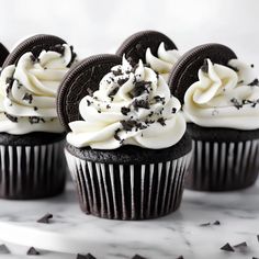 four chocolate cupcakes with white frosting and oreo cookies on the top