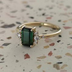 an emerald and diamond ring sitting on top of a table