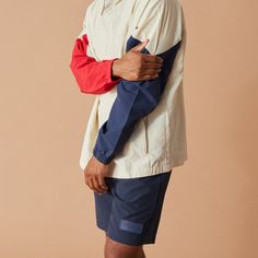 a man with his arms crossed standing in front of a beige background wearing shorts and a white jacket