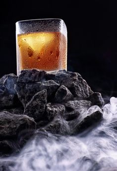 a glass filled with liquid sitting on top of rocks next to some ice and water