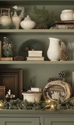 christmas decorations are displayed on the shelves in this green hutch with pine cones and evergreens