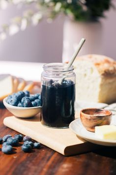 blueberries and bread on a cutting board next to a jar of jam with a spoon