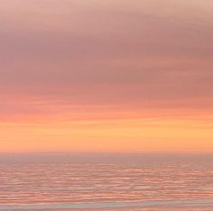 two people walking on the beach with surfboards under an orange and pink sky at sunset