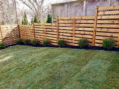 a wooden fence in the middle of a yard with grass and bushes on both sides