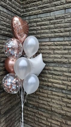 some white and gold balloons are in front of a brick wall with metallic foil on it