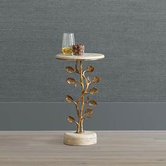 a table with two glasses on it and a gold leaf design stand in front of a grey wall