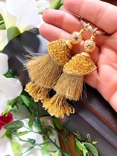 a pair of gold tasseled earrings on top of a black box with flowers in the background