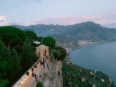 people are standing on the edge of a cliff overlooking water and mountains at dusk or dawn