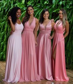 four women in pink dresses posing for the camera with greenery on the wall behind them