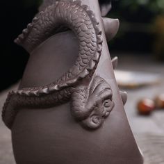 a close up of a vase with a snake on it's head and other items in the background