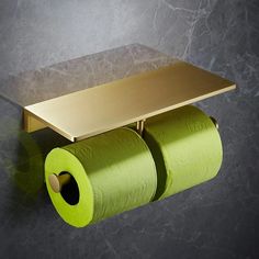 two rolls of toilet paper are hanging on the wall next to a gold plated shelf