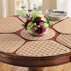 a round table with place mats on it and flowers in the center surrounded by wine glasses