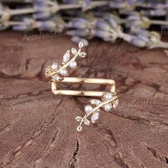 two gold rings with pearls and leaves on top of a piece of wood next to lavender flowers