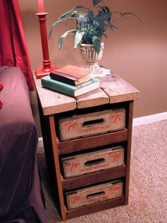 a wooden table topped with three drawers next to a lamp and a red bed sheet