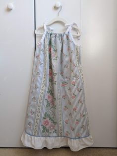 "Your child will feel cool and comfortable all summer long in this loose fitting sundress with adjustable tie straps. This dress features a small patch pocket on the front of the dress, ruffled hem, and a delicate, pastel blue and pink floral pattern. This listing is for the blue floral sundress as shown in the thumbnail. The blue check dress on the model is only to show the fit of the dress. This dress is listed as size 5-7, but please be sure to check the measurements, and keep in mind that th Cotton Sundress With Tie And Ruffled Straps, Summer Ruffle Dress For Sleepover, Summer Ruffled Dress For Sleepover, Cotton Sundress With Ruffled Straps, Cotton Sundress With Tie Back And Ruffled Straps, Cute Sundress With Ruffled Straps For The Beach, Cute Sundress With Ruffled Adjustable Straps, Cotton Sundress With Ruffled Straps For Garden Party, Pink Cotton Sundress With Adjustable Straps