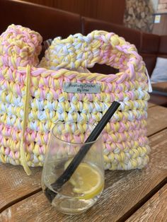 a crocheted basket and glass on a wooden table with a straw in it