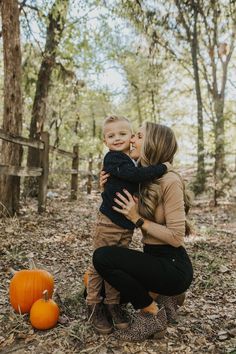 a woman holding a baby in her arms while sitting on the ground next to pumpkins