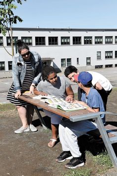 four people are gathered around a table with books on it and one person is writing