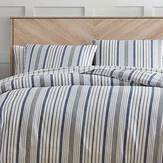 a bed with blue and white striped comforter on top of it next to a wooden headboard