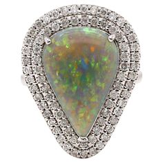 14CT White Gold Australian Opal And Diamond Cocktail Ring This stunning cocktail ring features a pear cabochon-cut Australian Opal from Mintabie, renowned for its vivid play of color. The Opal's unique surface displays a mesmerizing dance of vibrant hues, including shades of electric blue, fiery orange, and green, which shift and change as light hits it from different angles. Surrounding the opal is a luxurious setting of seventy-four round brilliant cut diamonds, enhancing the Opal's vibrant co Cocktail Ring Designs, Diamond Cocktail Ring, Bracelet Love, Diamond Cocktail Rings, Shopping Photography, Modern Ring, Loose Stones, Orange And Green, Dress Rings