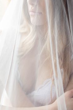 a woman wearing a wedding veil looking out the window at something else in her hand