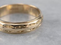 a gold wedding band with intricate designs on the inside and outside, sitting on a gray surface