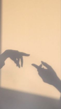 two hands pointing at each other in front of a wall with the shadow of someone's hand on it