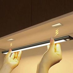 two hands reaching up to the ceiling with lightning bolt lights above them, and one person's hand holding an electronic device in their left hand