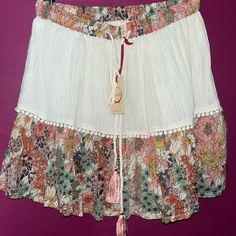 Raga Nwt Mini Skirt Love This It Has A Cream Too With Gold Strands Through The Material With A Floral Bottom. There Are Embellishments At The Fabric Split Line. Love! It Is The Gauze Material But Able Layered. Bohemian Short Mini Skirt For Spring, Casual Spring Shorts With Tassels, Casual Tassel Shorts For Spring, Spring White Skirt With Tassels, White Bohemian Mini Skirt With Floral Print, Bohemian White Mini Skirt With Floral Print, White Tassel Skirt For Spring, Summer Cotton Skirt With Tassels, Multicolor Bottoms With Tassels For Spring