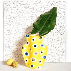 a yellow vase sitting next to a green leaf on top of a white countertop