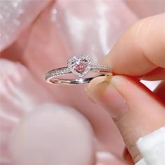 a close up of a person's hand holding a ring with a pink diamond