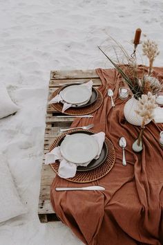 a table set up on the beach with plates and utensils