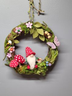 a wreath with mushrooms, grass and flowers hanging on the wall in front of a gray wall