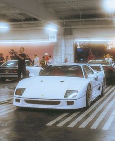 two white sports cars parked in a parking garage while people watch from the other side