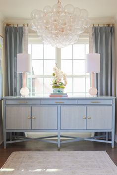 a blue dresser with two lamps and a chandelier hanging from it's ceiling