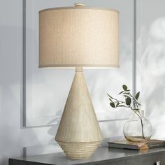 a table lamp sitting on top of a dresser next to a vase with a plant in it