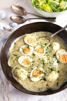 a bowl filled with soup and eggs on top of a table next to a salad