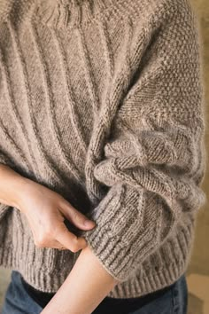 a woman wearing a sweater and jeans is holding her stomach