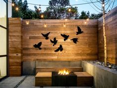 a fire pit with birds flying over it and lights strung from the wall behind it