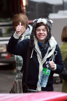 a young man wearing a furry hat and holding a water bottle giving the thumbs up