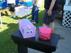 a woman standing next to a pink and purple box on top of a black table