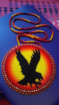 an eagle beaded onto a blue case on a pink surface with a red and yellow background