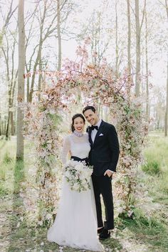 a bride and groom pose for a photo in front of an archway with pink flowers