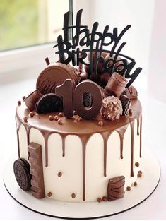 a birthday cake with chocolate icing and decorations on it's top is displayed in front of a window