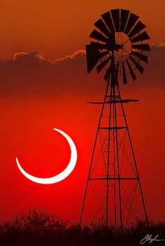 the sun is setting behind a windmill with a crescent moon in the sky above it