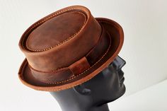 Introducing our handmade, genuine leather hat in a beautiful shade of brown.  The Classic Pork Pie style gives this hat a timeless, elegant look.  Crafted from high-quality leather, this hat is not only stylish but also durable and long-lasting.  Each hat is made by hand, ensuring that every piece is unique and of the highest quality. Perfect for both casual and formal occasions, this hat is a versatile addition to any wardrobe.  Its classic design is sure to never go out of style and it's a mus Classic Brown Top Hat With Flat Brim, Classic Brown Handmade Hat, Brown Fitted Top Hat With Flat Brim, Fitted Brown Top Hat With Flat Brim, Fitted Brown Brimmed Top Hat, Fitted Brown Top Hat With Short Brim, Classic Brown Hat With Flat Crown, Rustic Brown Top Hat With Flat Brim, Rustic Brown Top Hat With Curved Brim