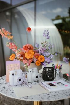 a table topped with flowers and cameras next to a notebook on top of a table