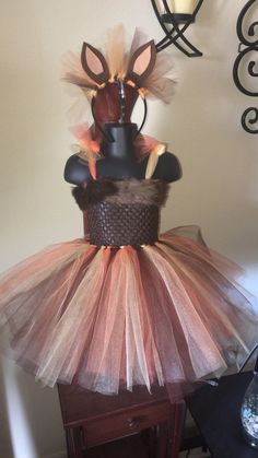 a dress made out of tulle and fabric on top of a wooden table next to a lamp