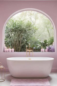 a white bath tub sitting under a window next to a lush green plant filled wall