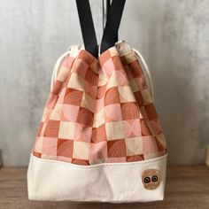 an orange and white checkered bag hanging from a hook on a wooden table with black straps